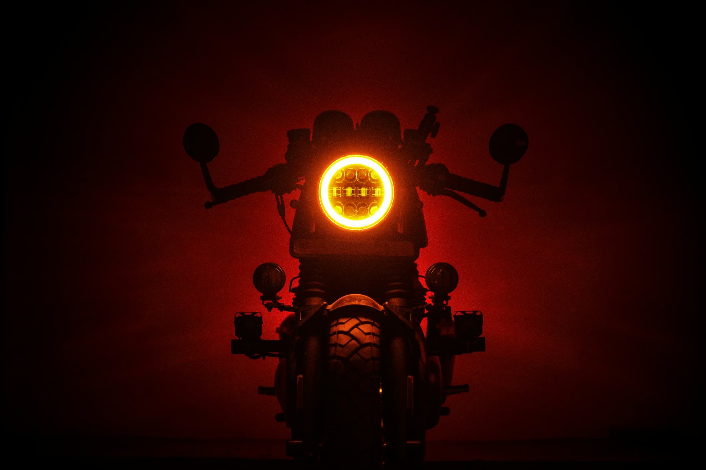 Silhueta de uma moto custom no escuro, farol redondo aceso em laranja.